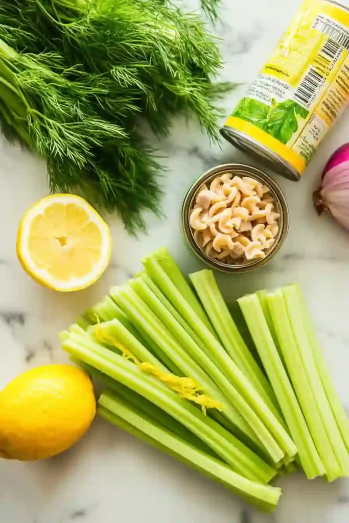 Zesty Lemon-Dill Tuna Pasta Salad Even Kids Love 2 Flat lay of ingredients for tuna pasta salad: fresh dill, lemons, celery, red onion, and a can of tuna.